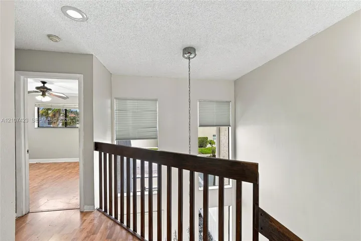 Landing area featuring wood-finish flooring, recessed lighting, a stained wood railing, and dual vertical windows