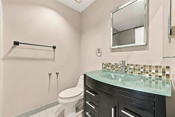 Vanity featuring a dark wood-finish cabinet, glass countertop with integrated basin, and mosaic tile backsplash, accented by a chrome faucet and framed mirror