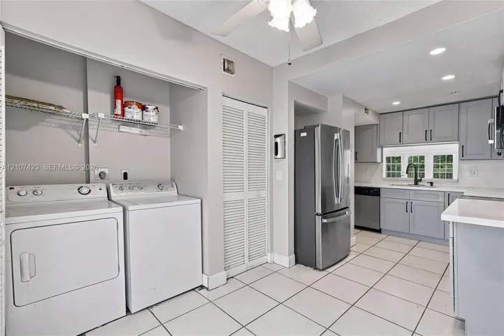 Kitchen and laundry area featuring grey cabinetry, stainless steel appliances, white tile flooring, louvered closet doors, and wire shelving
