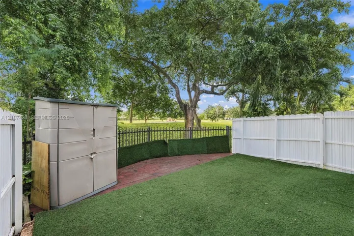 Backyard featuring synthetic turf, white vinyl privacy fencing, metal perimeter railing, and mature trees
