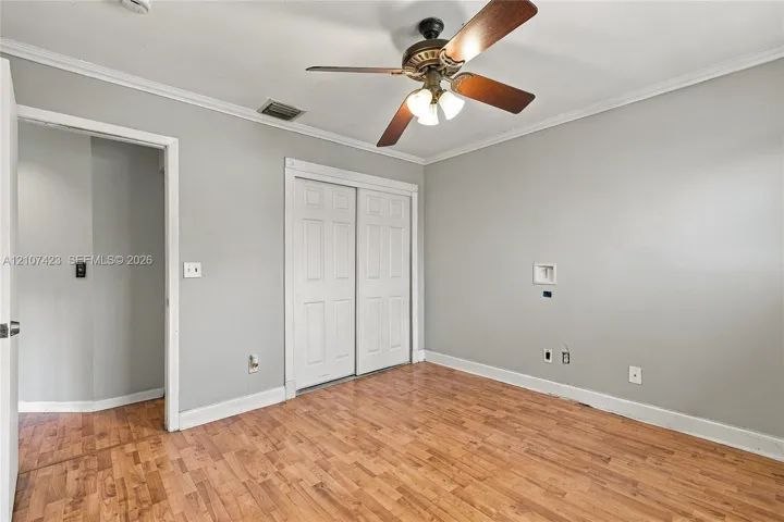 Interior space featuring wood-finish flooring, crown molding, a central ceiling fan with integrated lighting, and a double-panel closet door