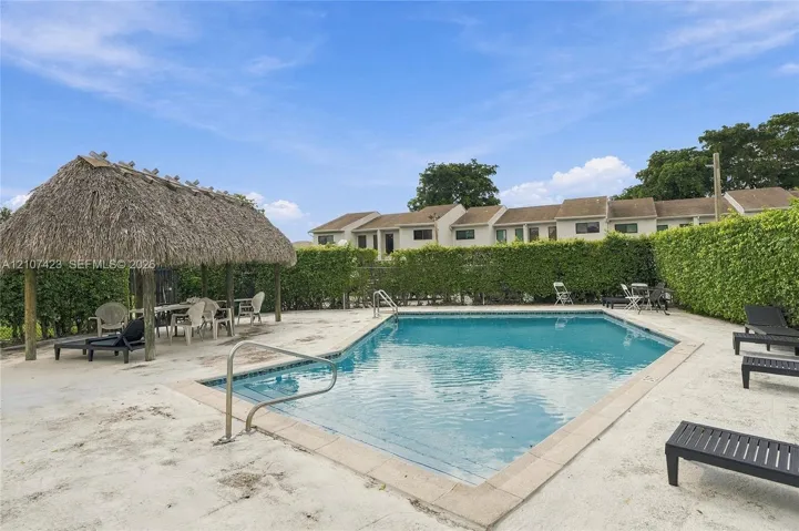 Swimming pool with a metal handrail, thatched-roof cabana, and perimeter privacy hedging