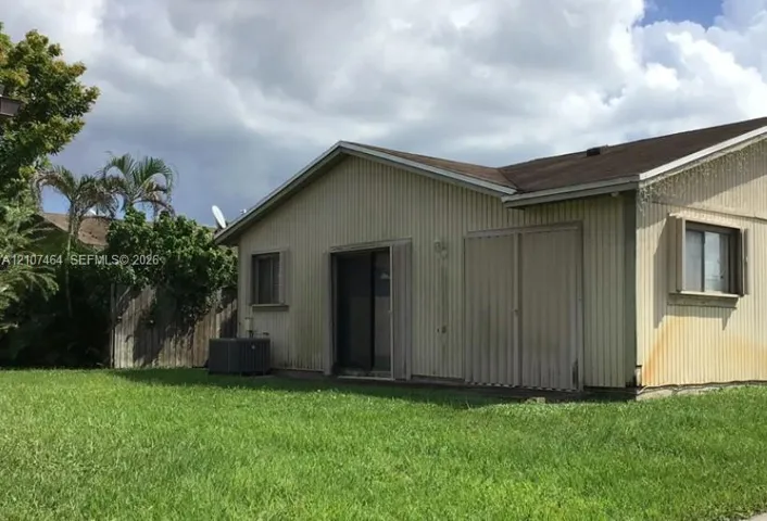 Exterior elevation featuring vertical metal siding, a gabled roofline, sliding glass door, and a grass lawn