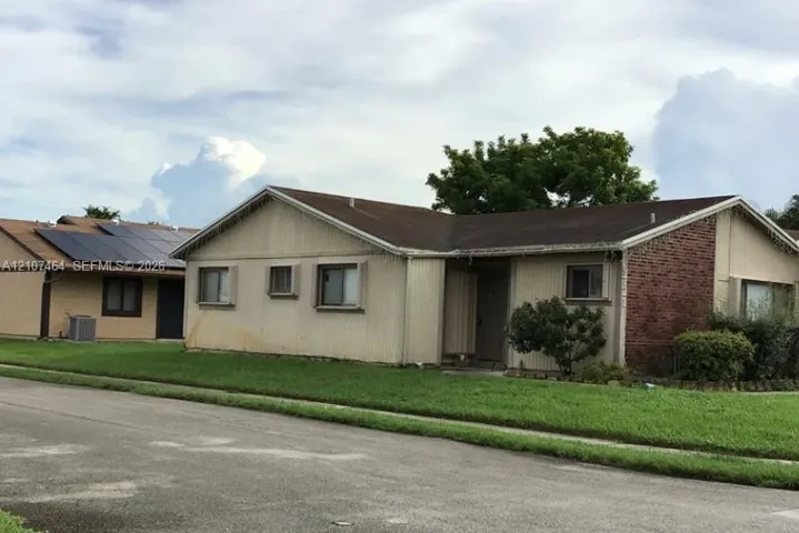 Single-story residence featuring vertical siding, a brick facade accent, a shingled roof, and an integrated solar panel system