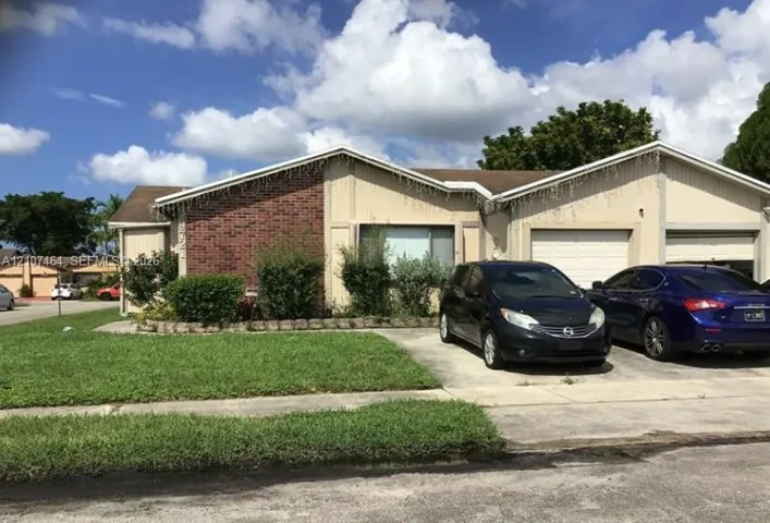 Single-story exterior featuring a brick facade, vertical wood-panel siding, dual-gabled roofline, two-car garage, and concrete driveway