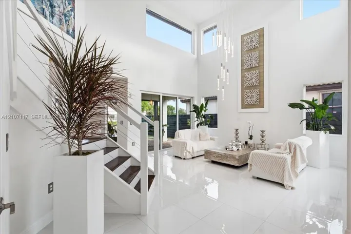 Double-height living area featuring floor-to-ceiling walls, polished oversized tile flooring, a multi-tiered glass pendant light fixture, and a staircase with a white-finished railing and wood-finish treads