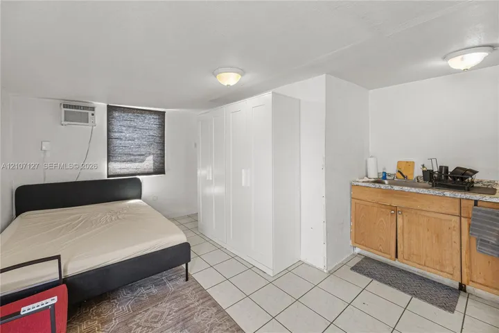 Interior space featuring white tile flooring, built-in white cabinetry, and a kitchenette with wooden cabinetry and a stone-finish countertop