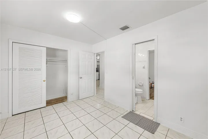 Ceramic tile flooring, closet with louvered bi-fold doors, six-panel interior door, and flush-mount ceiling lighting