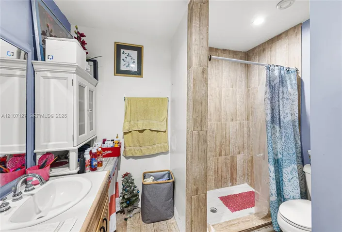 Bathroom featuring a shower stall with stone-finish tile surround and a vanity with a white basin and integrated storage cabinet