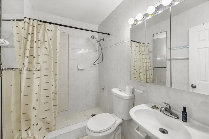 Full bathroom featuring floor-to-ceiling tile, a walk-in shower with a handheld fixture, an integrated medicine cabinet mirror, and a wall-mounted vanity sink with a multi-bulb light fixture