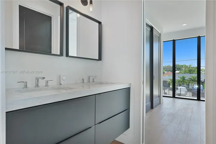 Floating vanity with dual-basin stone countertop, wall-mounted matte black-framed mirrors, wood-finish flooring, and floor-to-ceiling windows