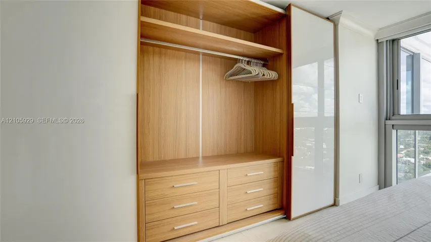 Built-in floor-to-ceiling wardrobe featuring wood-finish cabinetry, six integrated drawers, overhead shelving with a clothing rod, and a sliding glass door panel