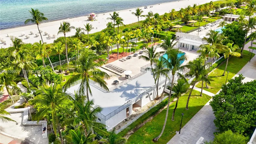 Oceanfront grounds featuring a swimming pool, paved sundeck, expansive lawn, mature palm trees, and direct beach access