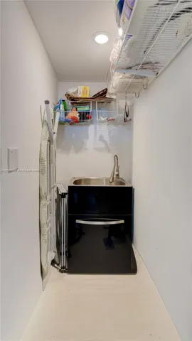 Utility area featuring a stainless steel drop-in sink, high-arc pull-down faucet, black cabinetry, and built-in wire shelving