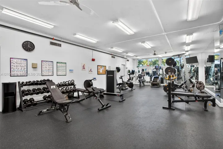 Fitness center featuring rubberized flooring, linear fluorescent lighting, ceiling-mounted fans, and full-length wall mirrors