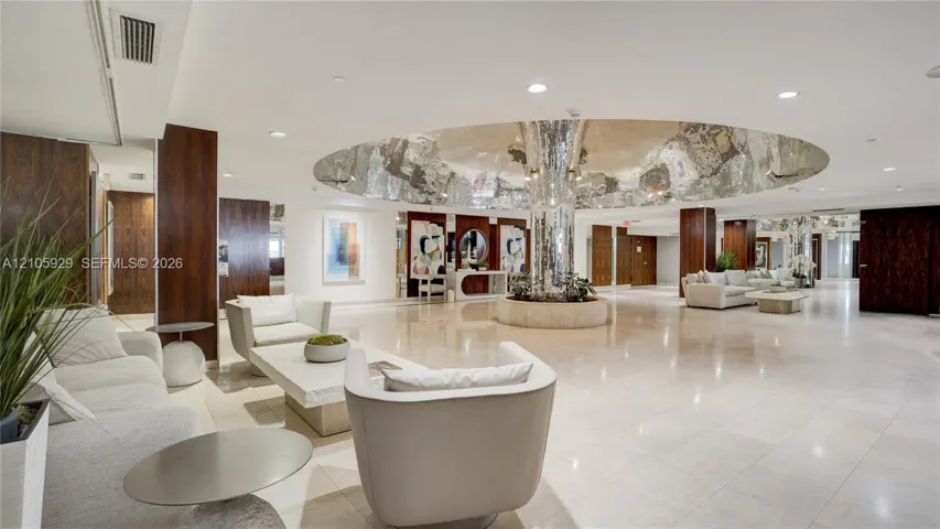 Expansive lobby featuring polished stone flooring, dark wood-finished paneling, recessed lighting, and a prominent central circular ceiling feature with a reflective metallic finish