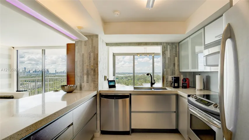 Kitchen featuring stainless steel appliances, flat-panel cabinetry with glass-front uppers, solid surface countertops, a textured stone backsplash, and floor-to-ceiling windows