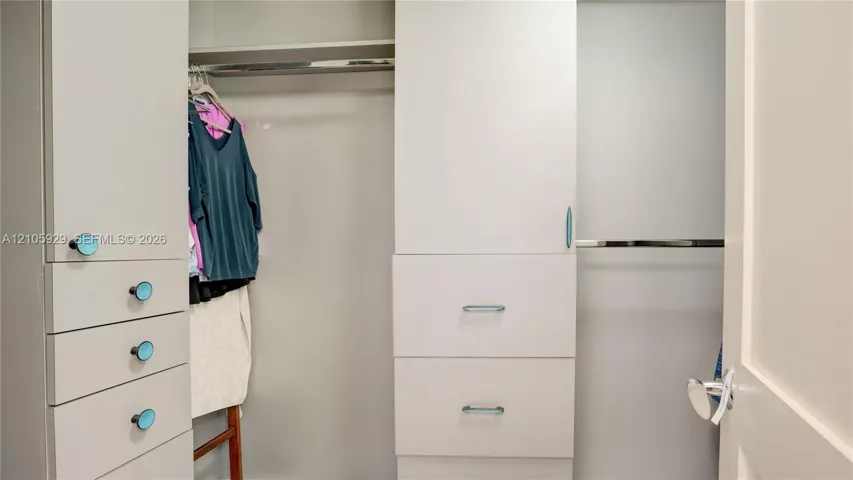 Custom built-in closet organization system featuring white cabinetry, multiple storage drawers, dual hanging rods, and integrated shelving