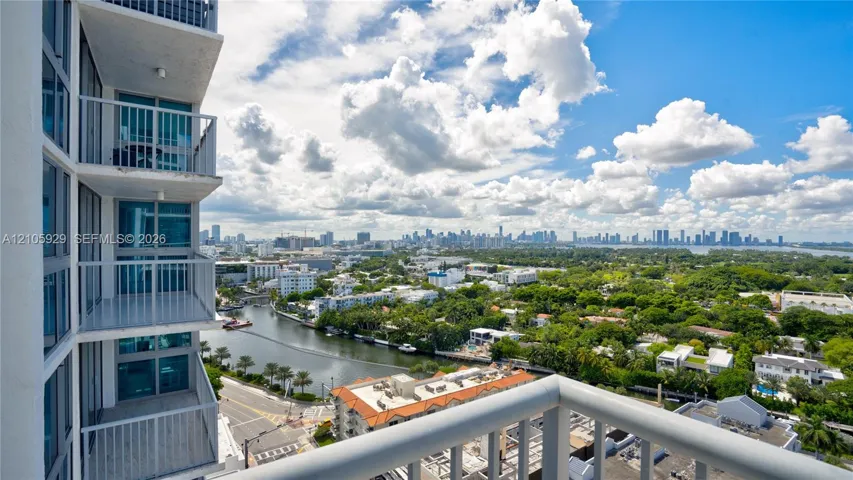 High-rise balcony featuring metal railings and floor-to-ceiling glass paneling, overlooking the surrounding cityscape and waterway