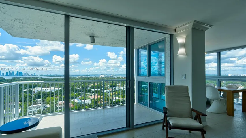 Floor-to-ceiling glass sliding doors, wrap-around covered balcony with metal railing, tile flooring, and architectural wall sconce