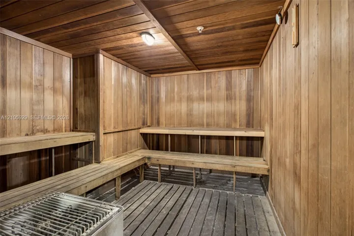 Sauna featuring tongue-and-groove wood wall paneling, multi-level wood bench seating, wood slat flooring, and an integrated heating unit