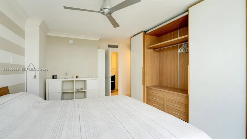 Built-in floor-to-ceiling wardrobe with sliding white panels, wood-finish interior shelving, and integrated drawers, featuring a modern three-blade ceiling fan and crown molding