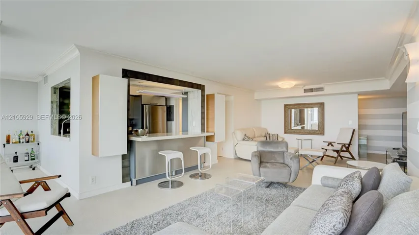Open-concept interior featuring a breakfast bar with stone-finish countertop, crisp crown molding, recessed lighting, and a built-in cabinetry surround