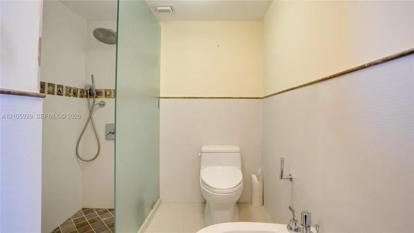 Walk-in shower featuring a frosted glass partition, rainfall showerhead, and tiled flooring, accompanied by a low-profile toilet and bidet