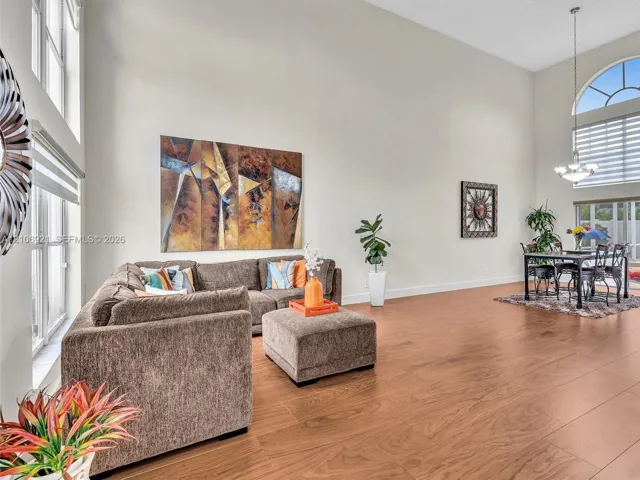 High-ceilinged interior space featuring wood-finish flooring, floor-to-ceiling windows, an arched window, and a multi-light chandelier