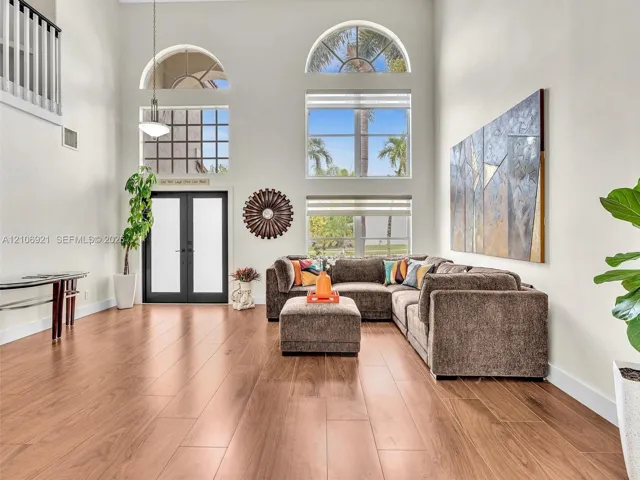 Expansive living space featuring soaring ceilings, wood-finish flooring, floor-to-ceiling windows with arched transoms, and a black-framed glass entry door