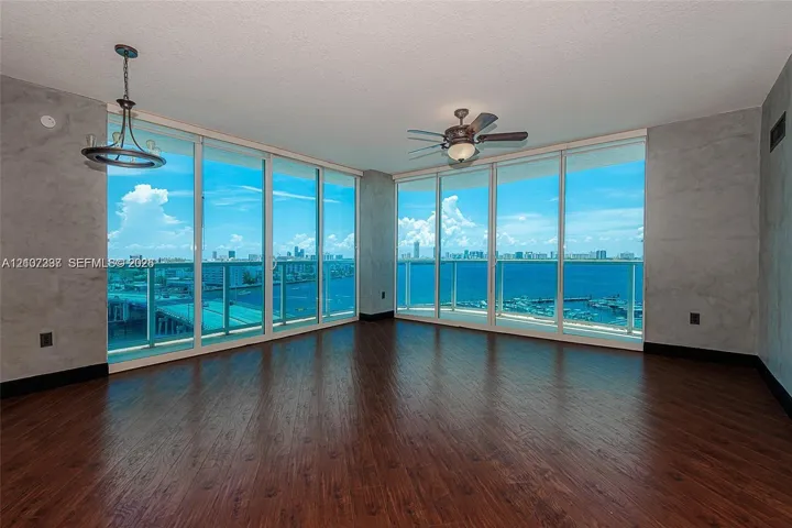 Floor-to-ceiling windows, wood-finish flooring, textured wall treatments, ceiling-mounted light fixture, and integrated ceiling fan