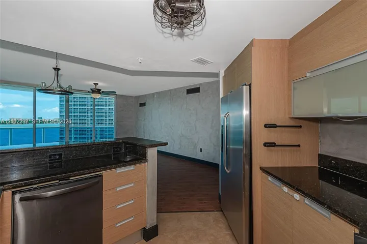 Kitchen featuring flat-panel wood cabinetry, dark stone countertops, stainless steel refrigerator, and industrial-style cage lighting
