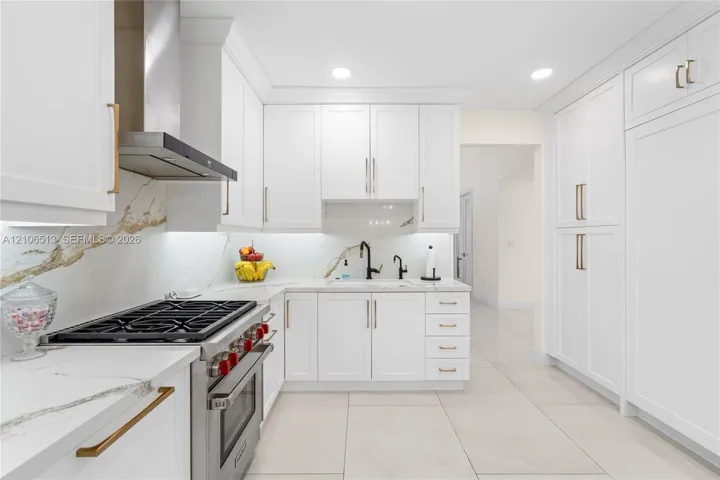 Kitchen featuring shaker-style white cabinetry, stone-finish countertops with matching full-height backsplash, stainless steel gas range with overhead vent hood, under-cabinet lighting, and large-format tile flooring