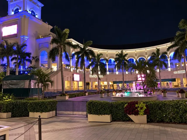 Neoclassical exterior featuring a multi-story clock tower, arched colonnades, decorative stone fountain, paver courtyard, and integrated landscape planters