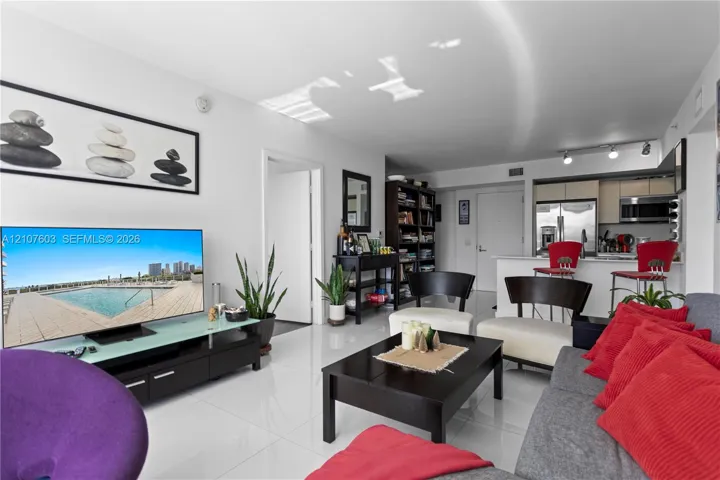 Open-concept living space featuring high-gloss tile flooring, recessed track lighting, and a kitchen peninsula with a white stone-finish countertop