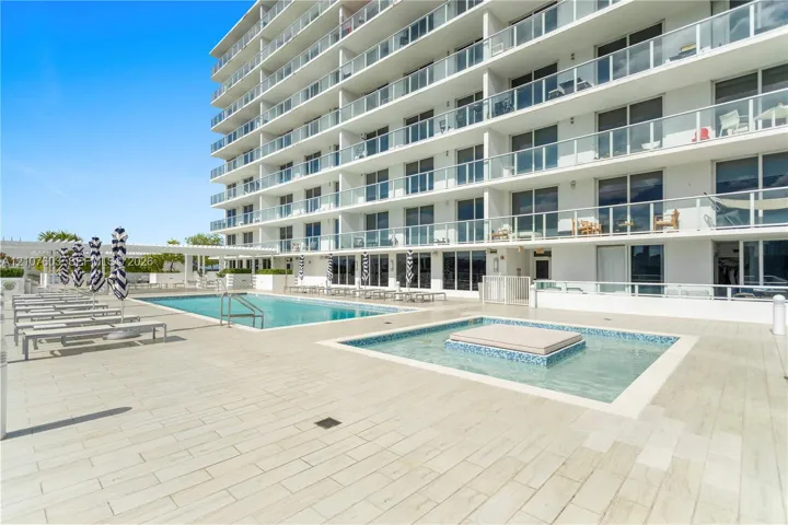 Poolside terrace featuring an in-ground swimming pool, tiled spa, wood-finish porcelain decking, and multi-story building exterior with glass-railed balconies