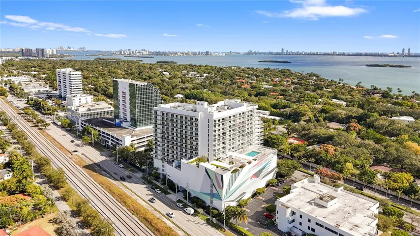 Aerial perspective featuring a mid-rise residential structure with a rooftop swimming pool and a prominent exterior geometric mural, located in a coastal setting