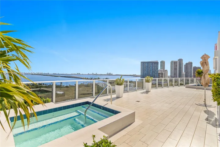 Expansive outdoor terrace featuring light-toned tile flooring, an in-ground spa with tile surround, and a glass-paneled railing