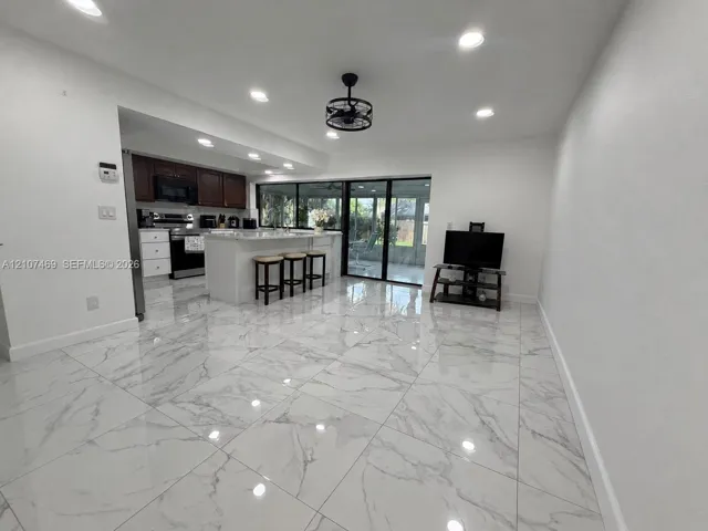 Large-format tile flooring with a marble-pattern finish, recessed ceiling lighting, industrial-style drum ceiling fan, kitchen island with a white countertop, and expansive sliding glass doors