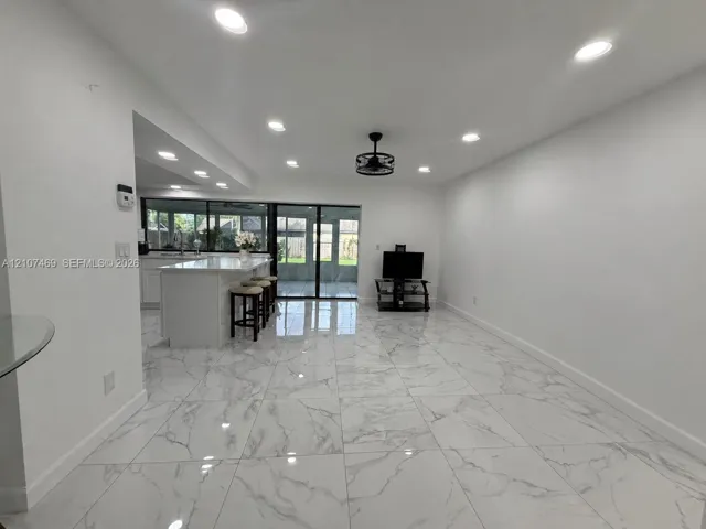Large-format porcelain tile flooring, recessed ceiling lighting, kitchen island with stone-finish countertop, and black-framed sliding glass doors