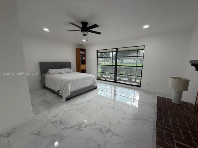 Large-format polished tile flooring, black-framed floor-to-ceiling windows, recessed lighting, matte black ceiling fan, and herringbone-patterned brick fireplace surround