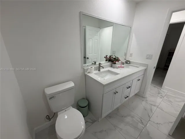 Double vanity featuring white cabinetry, stone-finish countertops, dual integrated sinks, and large-format tile flooring