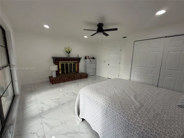 Room featuring large-format tile flooring, a brick fireplace with a mantle, recessed ceiling lighting, a ceiling fan, and double-door closets