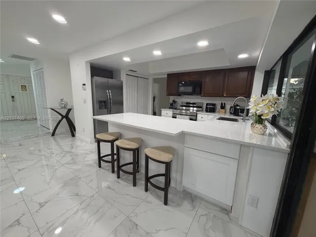 Kitchen featuring a quartz countertop island with a breakfast bar, stone-finish tile flooring, recessed lighting, and stainless steel appliances