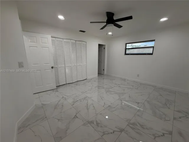 Large-format stone-finish tile flooring, white bi-fold closet doors, recessed ceiling lighting, and a multi-blade ceiling fan