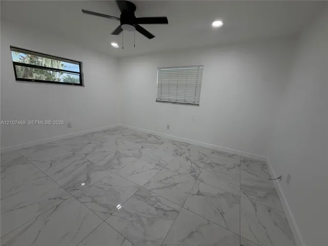 Large-format tile flooring, recessed ceiling lighting, and a modern ceiling fan, punctuated by two windows featuring horizontal blinds