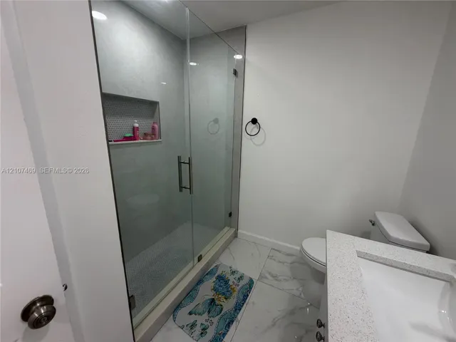 Walk-in shower with a glass enclosure, built-in tiled niche, stone-look tile flooring, and vanity with a rectangular sink and composite countertop