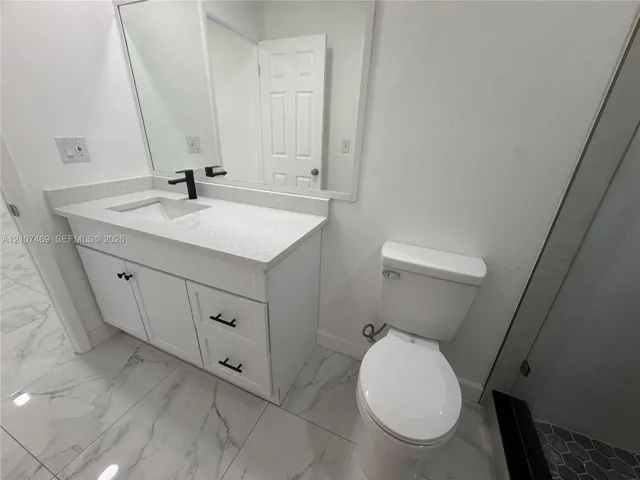 White vanity cabinet featuring a solid-surface countertop with an integrated basin, matte black hardware, a wall-to-wall mirror, and large-format porcelain tile flooring