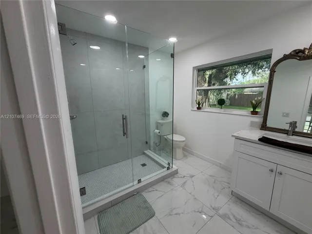 Walk-in shower featuring glass paneling and large-format tile surround, white cabinetry with countertop, and large-format flooring