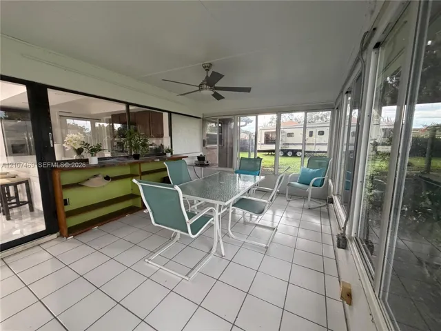Enclosed sunroom featuring white tile flooring, ceiling fan, and floor-to-ceiling glass panel walls
